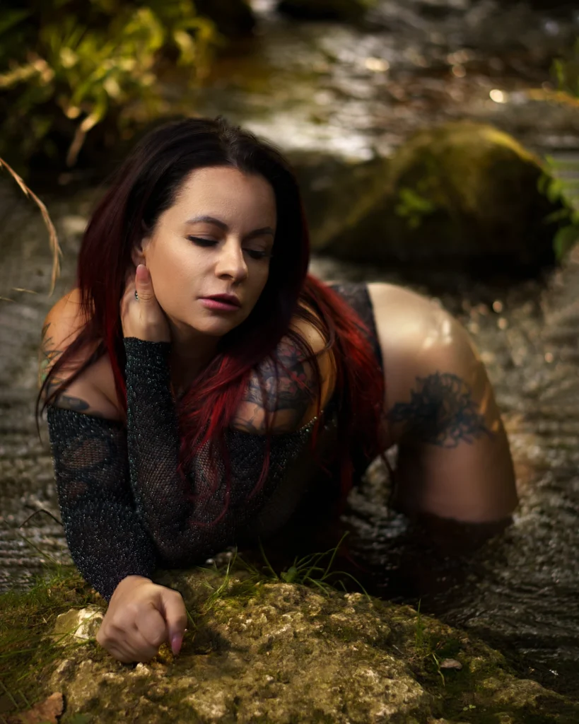 Outdoor Boudoir Shooting im Wasser Boudoir Fotografie in Bamberg – Frau liegt in einem Bach im Wald und trägt ein dunkles Dessous Outfit, natürliches Licht und Wasser erzeugen eine sinnliche Outdoor-Atmosphäre.